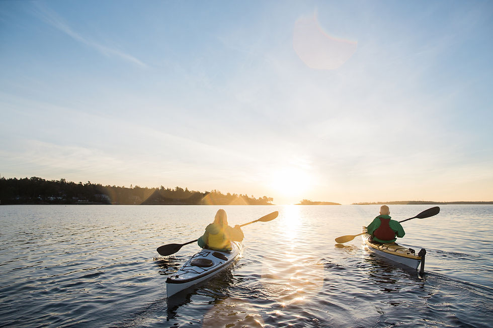 Two people kayaking on calm water toward a golden sunset
