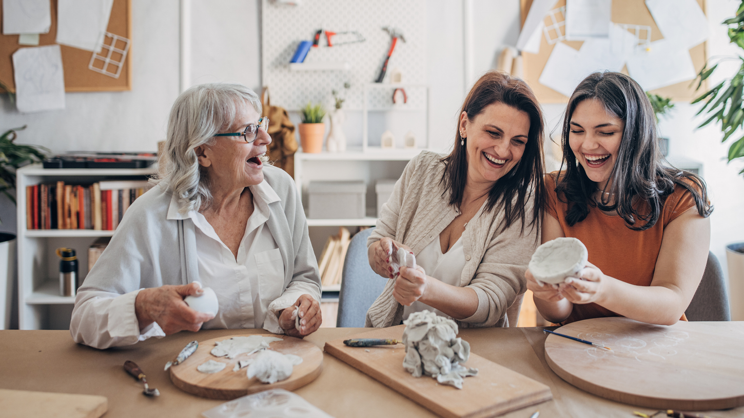 Three women laughing together while doing a craft activity indoors