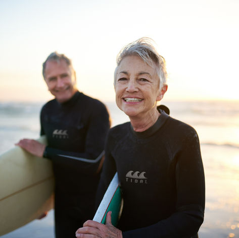 Senior couple holding surfboards at the beach at sunset