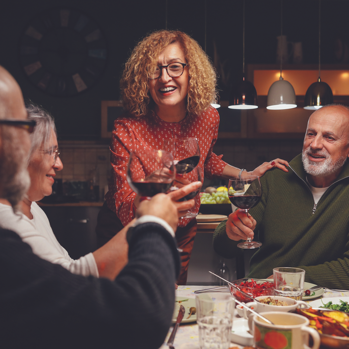 Group of cheerful adults laughing and toasting drinks at a dinner table with food