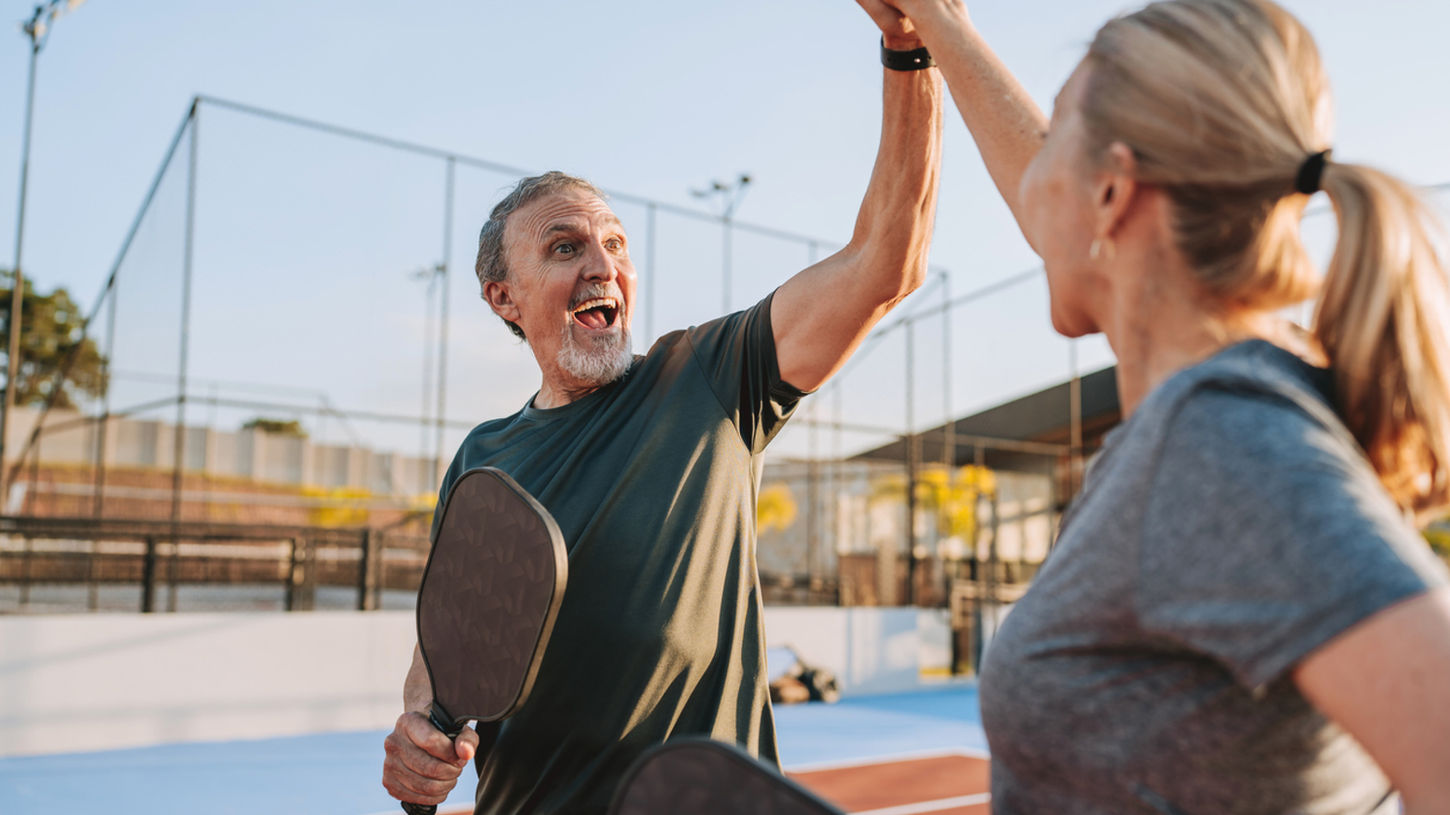 Smiling man and woman playing pickleball or tennis together at an outdoor court